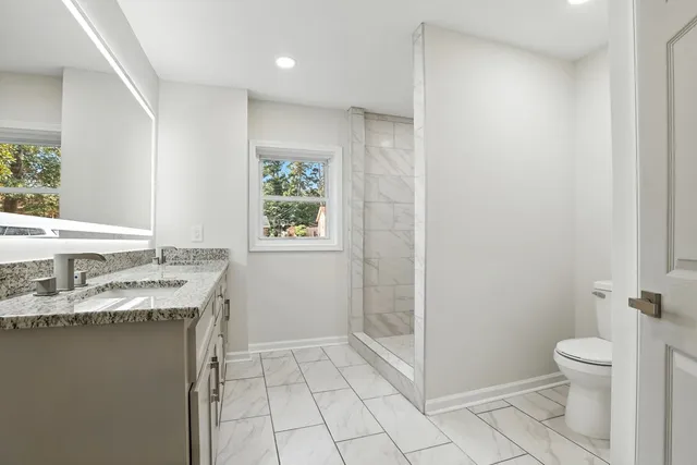 a bathroom with a granite countertop sink a toilet a mirror and shower
