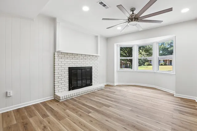 a view of an empty room with wooden floor fireplace and a window