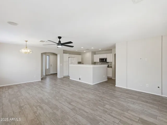 an empty room with wooden floor chandelier fan and windows