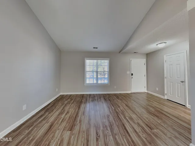 a view of an empty room with wooden floor and window