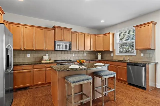 a kitchen with stainless steel appliances granite countertop a stove a sink dishwasher a microwave oven and a refrigerator with wooden cabinets