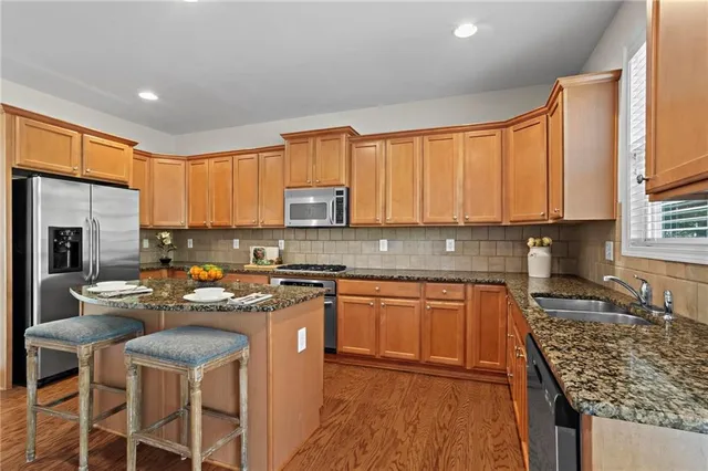 a kitchen with stainless steel appliances granite countertop a stove top oven a sink dishwasher and a refrigerator with wooden cabinets