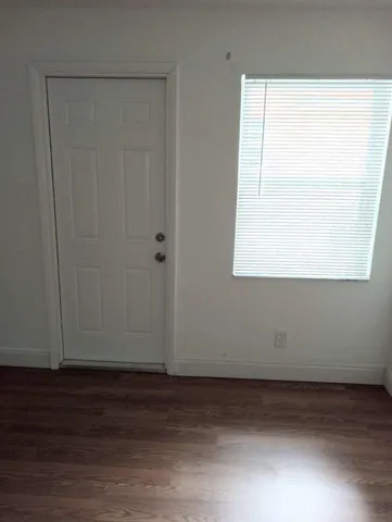 a view of an empty room with wooden floor and a window