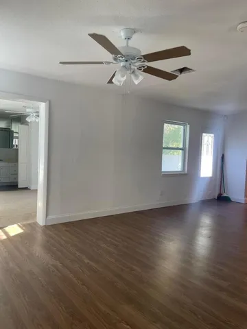 an empty room with wooden floor fan and windows