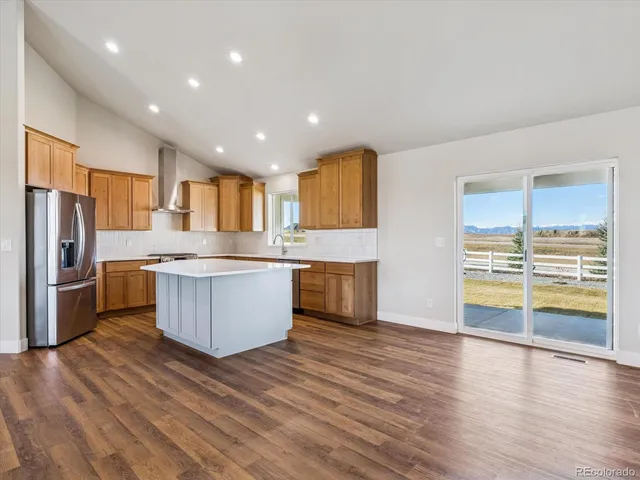 a large kitchen with stainless steel appliances granite countertop a stove a sink dishwasher a refrigerator and white cabinets with wooden floor