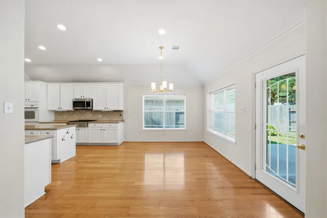 a large kitchen with kitchen island granite countertop a stove a sink a refrigerator and white cabinets with wooden floor