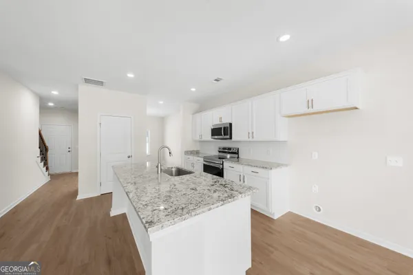 a large kitchen with kitchen island a stove a sink a refrigerator and white cabinets with wooden floor