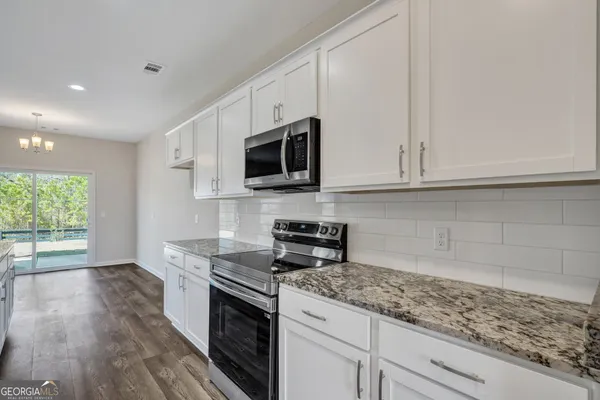 a kitchen with granite countertop white cabinets stainless steel appliances a sink and wooden floor
