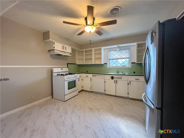 a kitchen with stainless steel appliances white cabinets a sink a stove a refrigerator and island with wooden floor