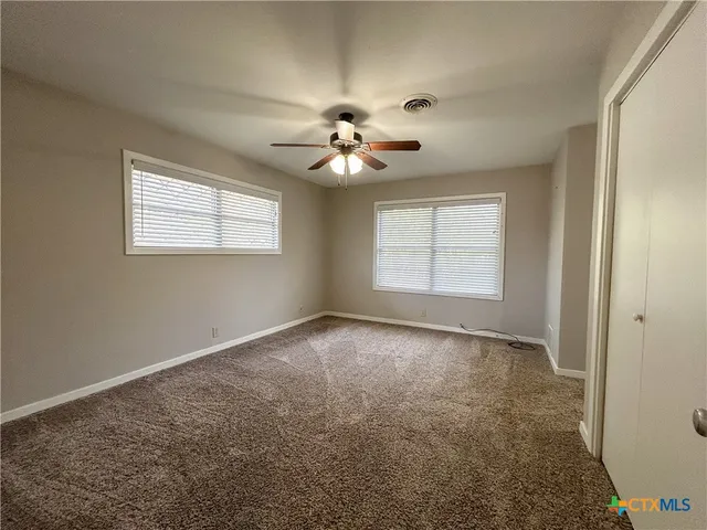 an empty room with windows and chandelier fan