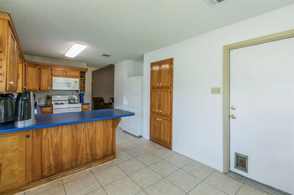 1936 Post Oak Drive Waco, TX 76705 - Photo 8 of 33 Kitchen featuring brown cabinets, a peninsula, white appliances, a textured ceiling, and light tile patterned floors
