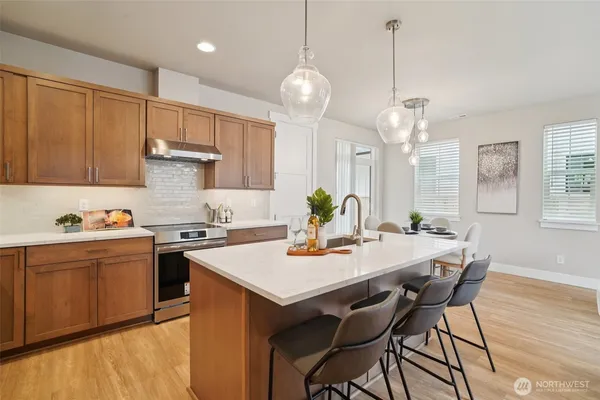 a kitchen with stainless steel appliances granite countertop a stove top oven a refrigerator a sink a dining table and chairs with wooden floor