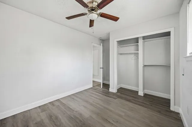 an empty room with wooden floor ceiling fan and window