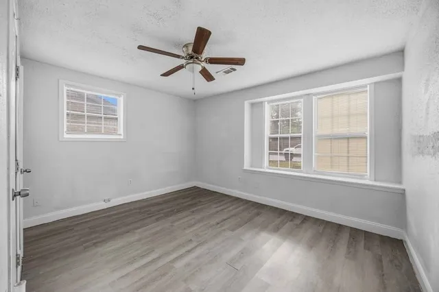 an empty room with wooden floor fan and windows
