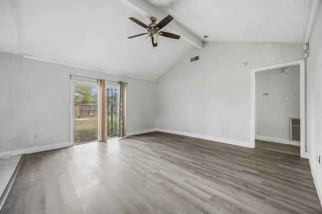 an empty room with wooden floor fan and windows