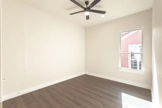an empty room with wooden floor fan and windows