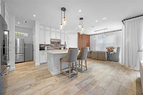 a kitchen with stainless steel appliances kitchen island granite countertop a refrigerator a stove a oven and white cabinets with wooden floor