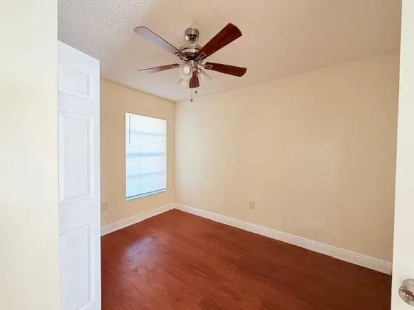 an empty room with wooden floor fan and windows