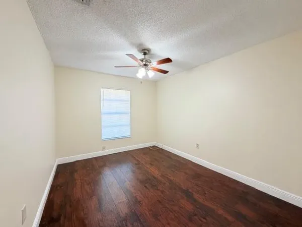 an empty room with wooden floor fan and windows