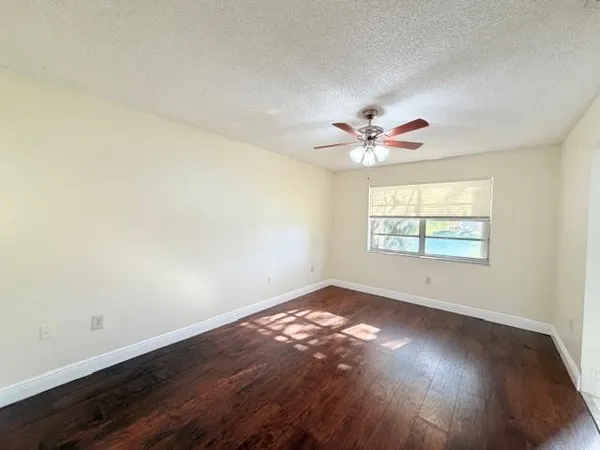 an empty room with wooden floor chandelier fan and windows
