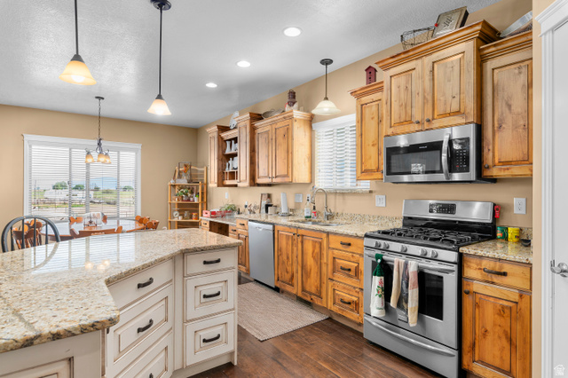 5702 950 North Ogden, UT 84404 - Photo 18 of 36 Open-concept kitchen featuring wood-finish cabinetry, granite-style countertops, stainless steel appliances, and a central island with white wood-finish cabinetry and pendant lighting