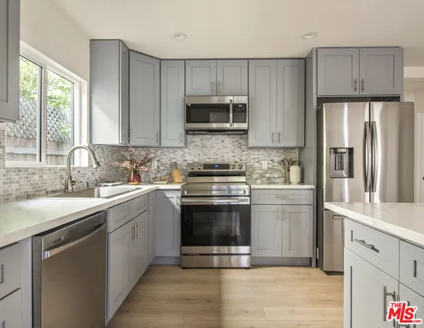 a kitchen with stainless steel appliances granite countertop a stove top oven a sink dishwasher and white cabinets with wooden floor