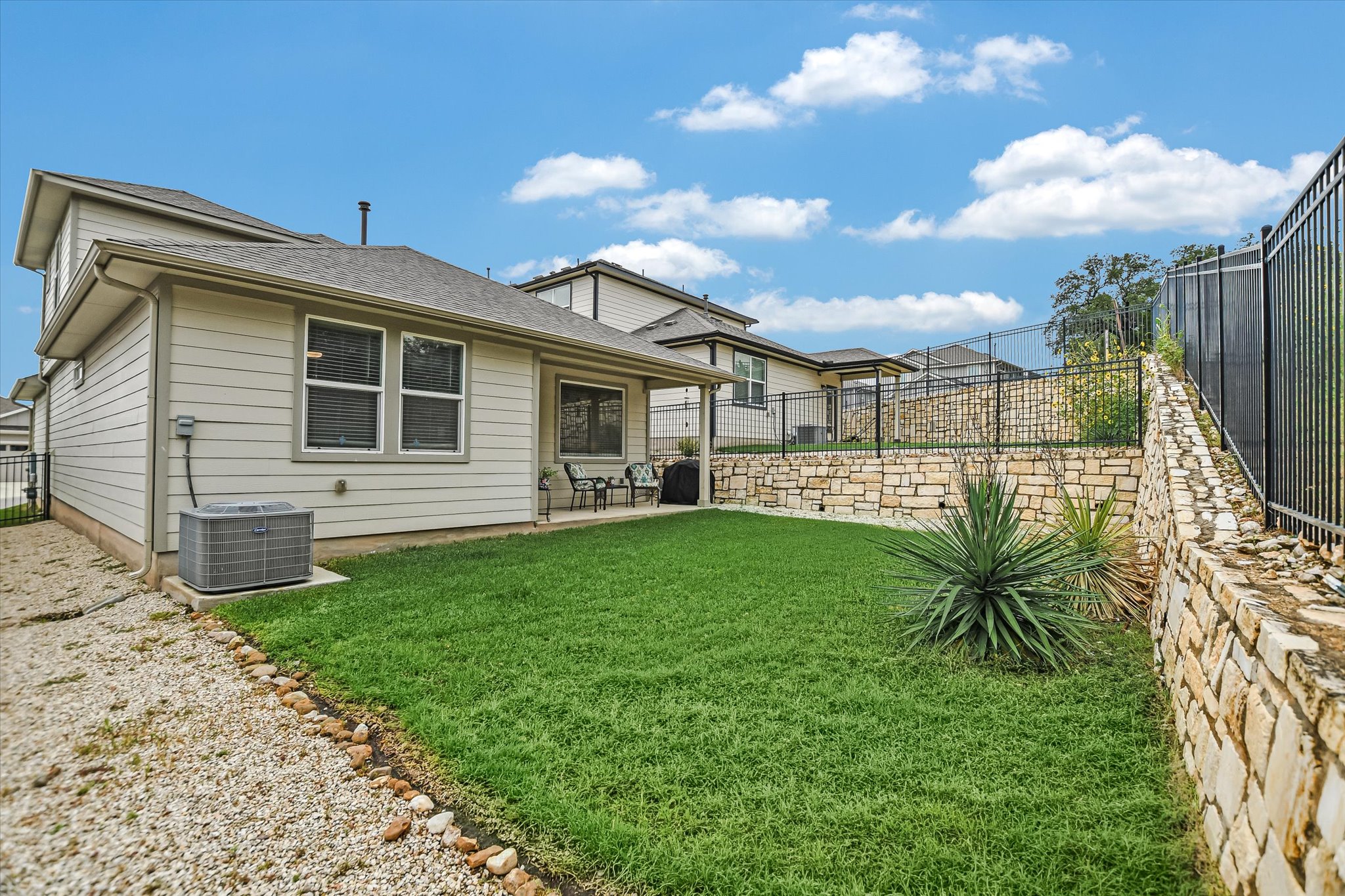 105 Merrick Road Georgetown, TX 78628 - Photo 20 of 23 A neatly maintained backyard features a grassy lawn, a cozy covered patio, and a charming stone retaining wall.