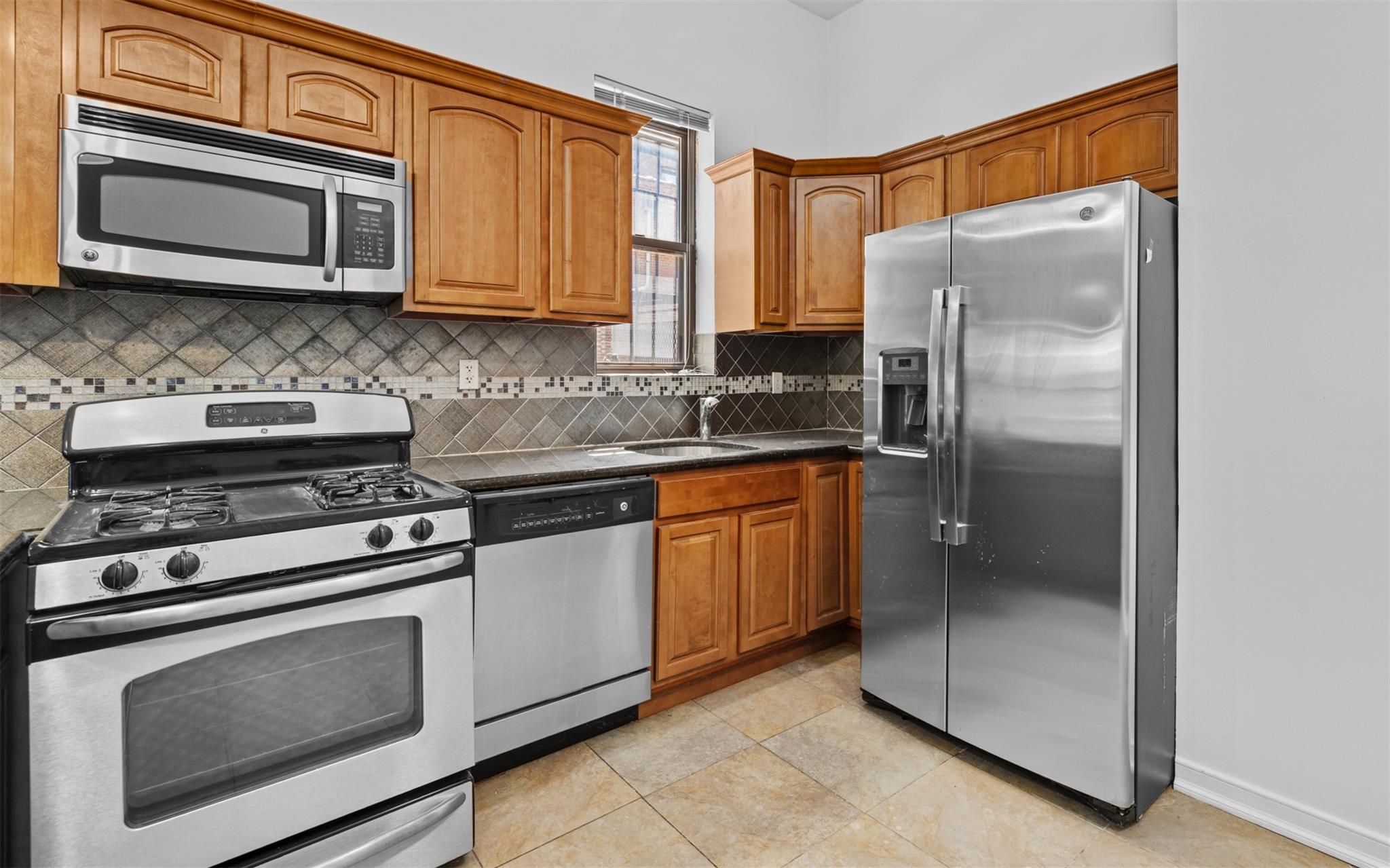 626 Madison Street Brooklyn, NY 11221 - Photo 15 of 42 Kitchen with appliances with stainless steel finishes, dark countertops, a sink, backsplash, and brown cabinetry