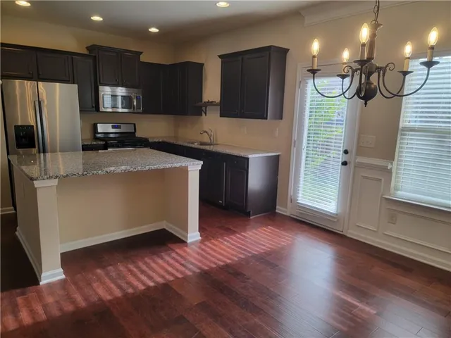 a kitchen with stainless steel appliances granite countertop a refrigerator a stove a sink and a microwave oven with wooden floor