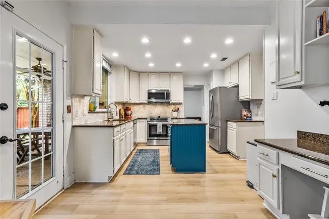 a kitchen with stainless steel appliances granite countertop a refrigerator a sink dishwasher a stove oven and a dining table with wooden floor
