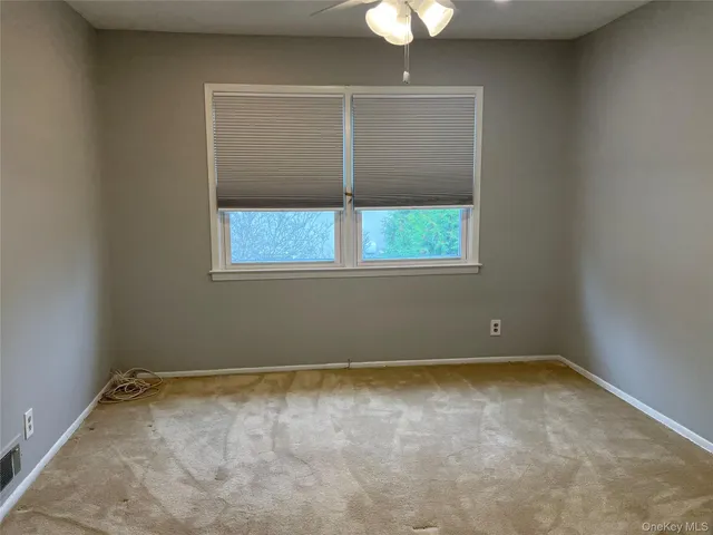 an empty room that has a chandelier fan and a window