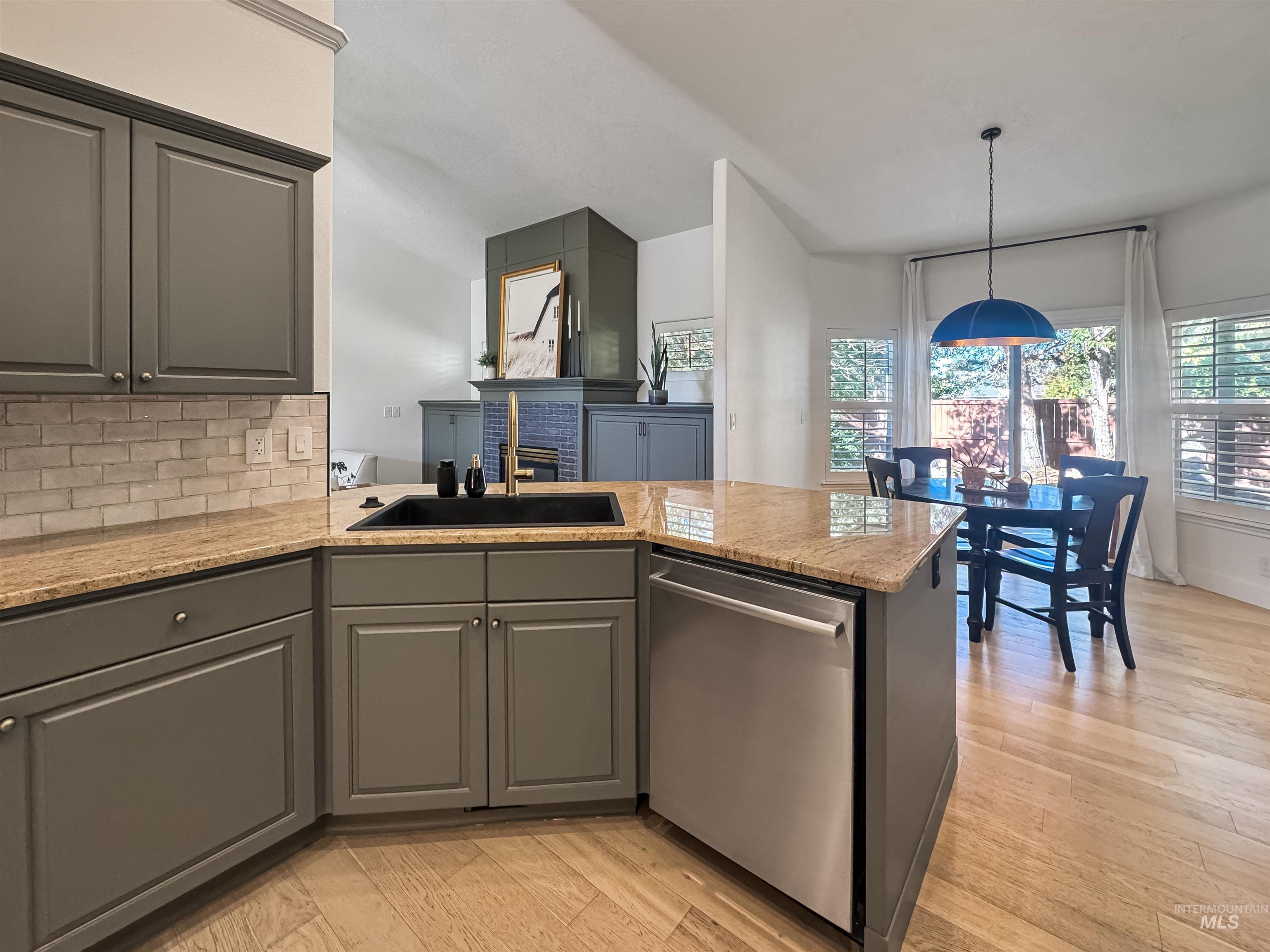 Kitchen featuring gray cabinetry, light granite countertops, a black sink with a gold-finish faucet, a stainless steel dishwasher, and a light wood-finish floor
