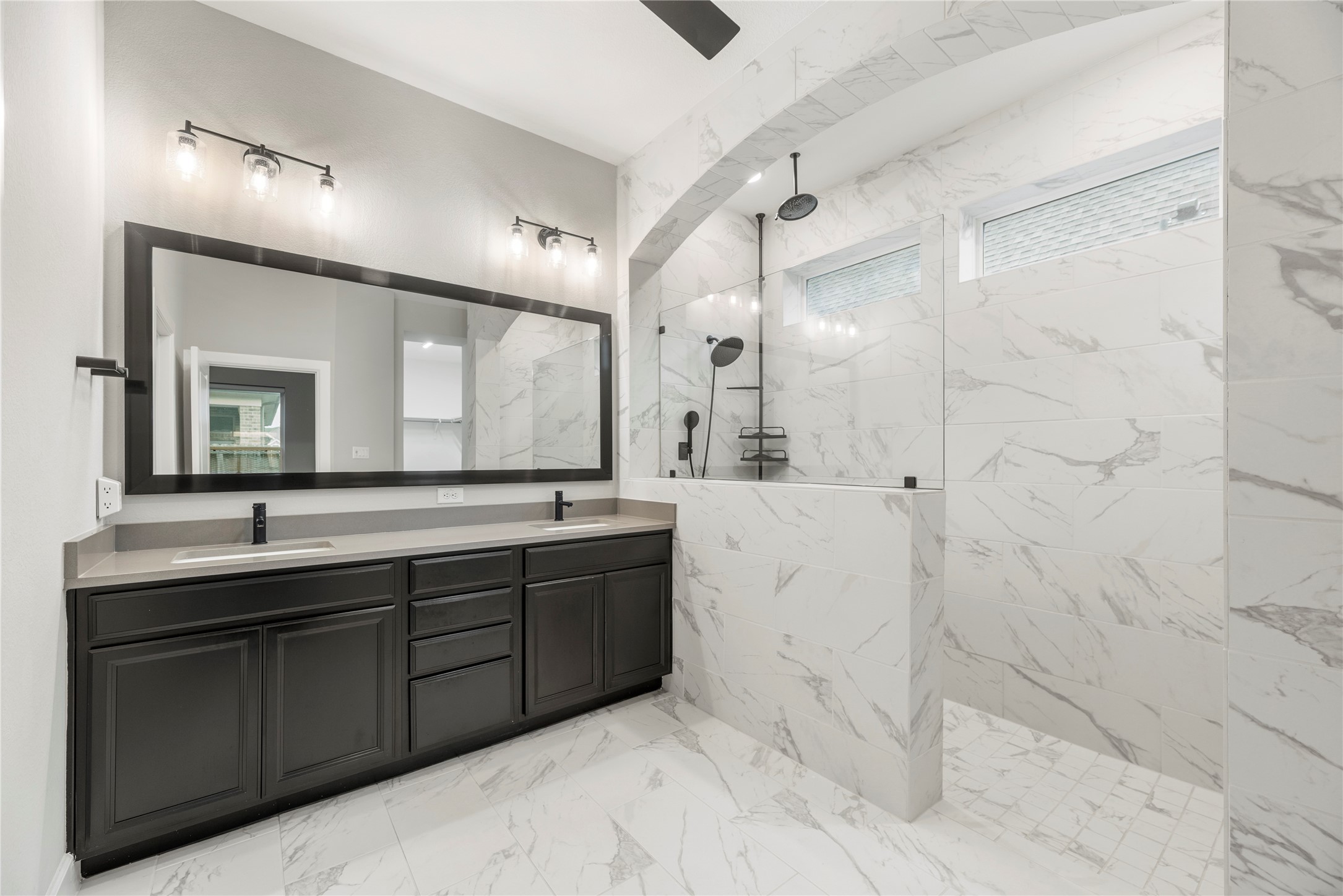 3438 Rich Radish Road Richmond, TX 77406 - Photo 10 of 25 The spa-like primary ensuite bathroom offers an abundance of preparation space, showcasing solid surface Lyra quartz countertops, dual sinks with matte black Moen Align faucets, a custom-framed mirror, and premium tile flooring.