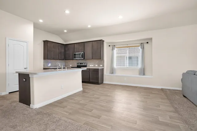 a kitchen with kitchen island granite countertop a stove top oven a sink and dishwasher with wooden floors