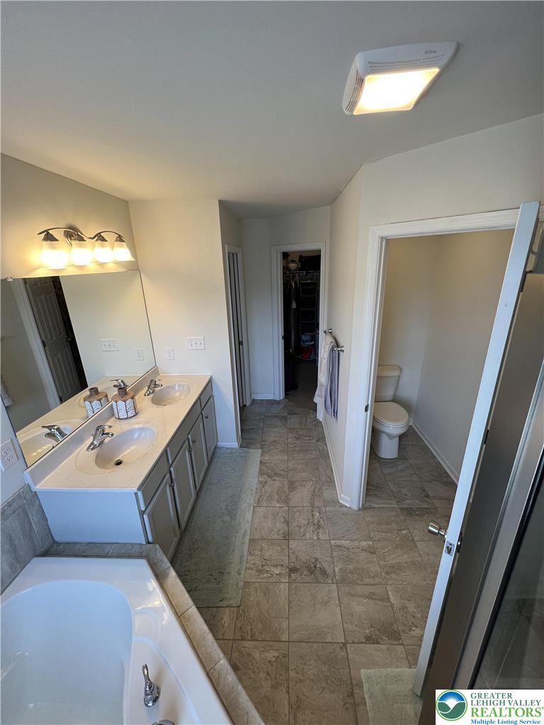 5380 Jutland Road Allentown, PA 18104 - Photo 20 of 27 A well-lit primary bathroom featuring a double vanity, soaking tub, and tile flooring.