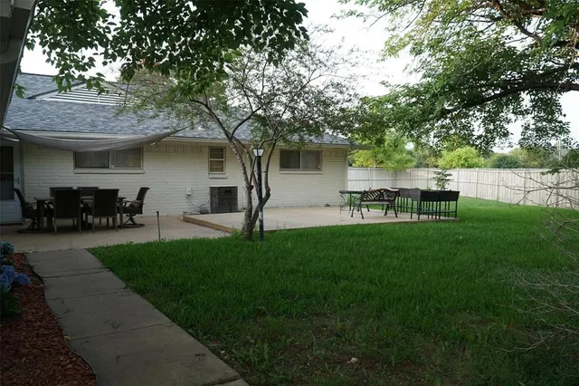 a view of a backyard with table and chairs potted plants and a large tree