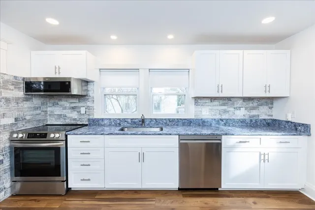 a kitchen with stainless steel appliances granite countertop a stove a sink and white cabinets