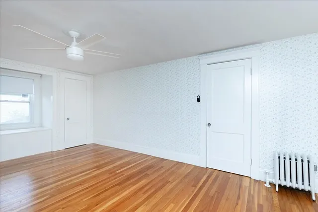 a view of empty room with wooden floor and fan