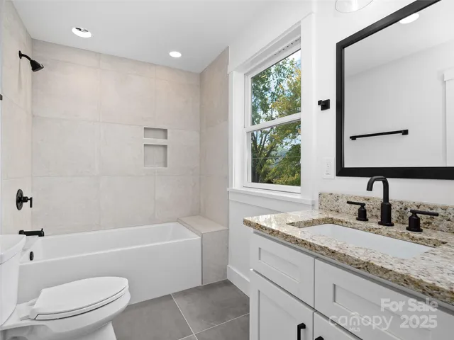 a bathroom with a granite countertop bathtub shower sink vanity mirror and toilet