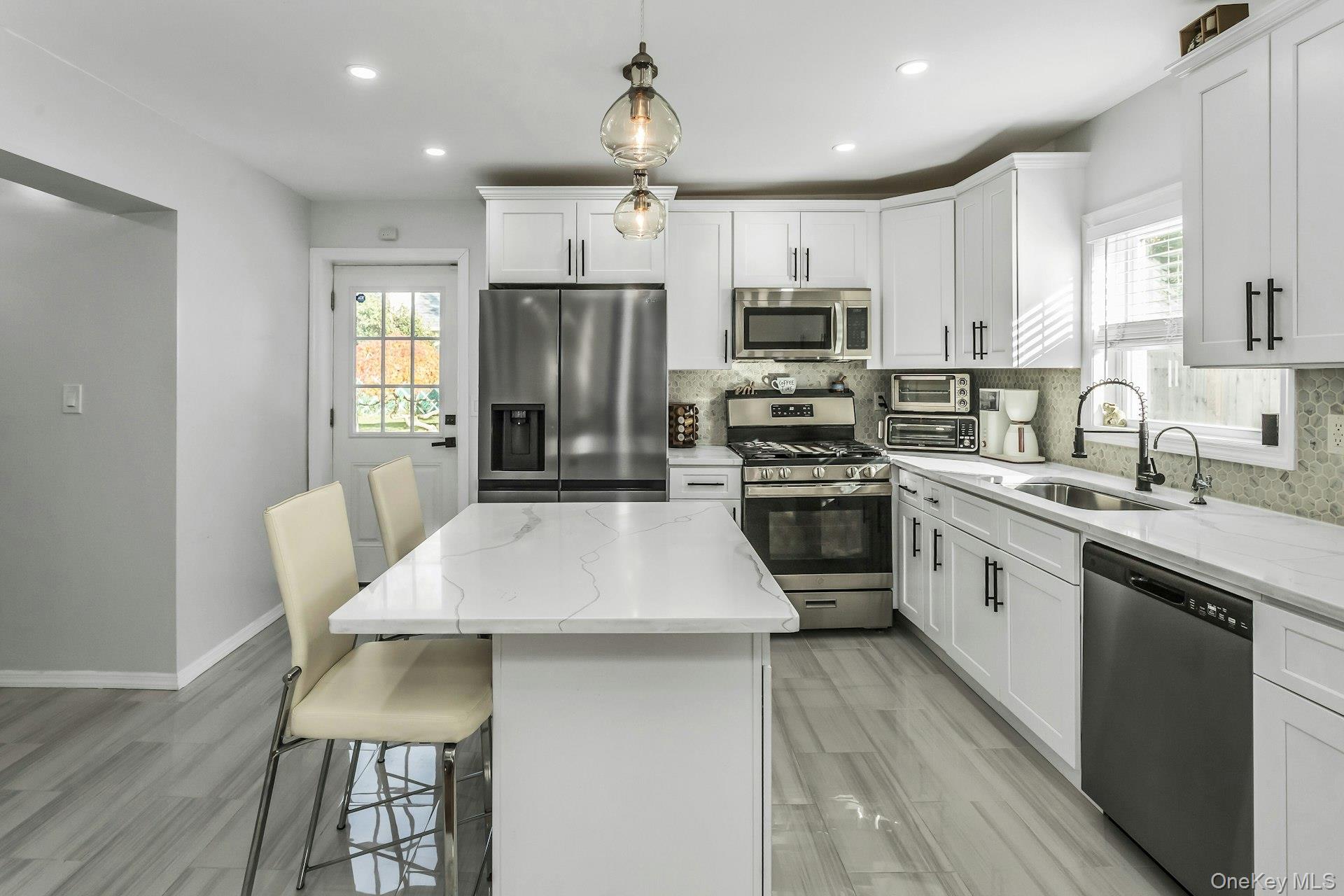 42 13th Street Locust Valley, NY 11560 - Photo 13 of 34 Kitchen featuring stainless steel appliances, tasteful backsplash, light stone counters, a breakfast bar area, and white cabinetry