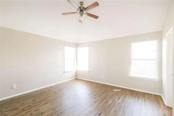 an empty room with wooden floor fan and windows