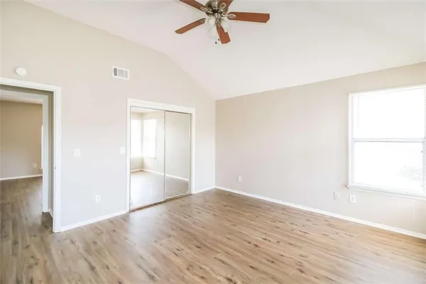 an empty room with wooden floor fan and windows