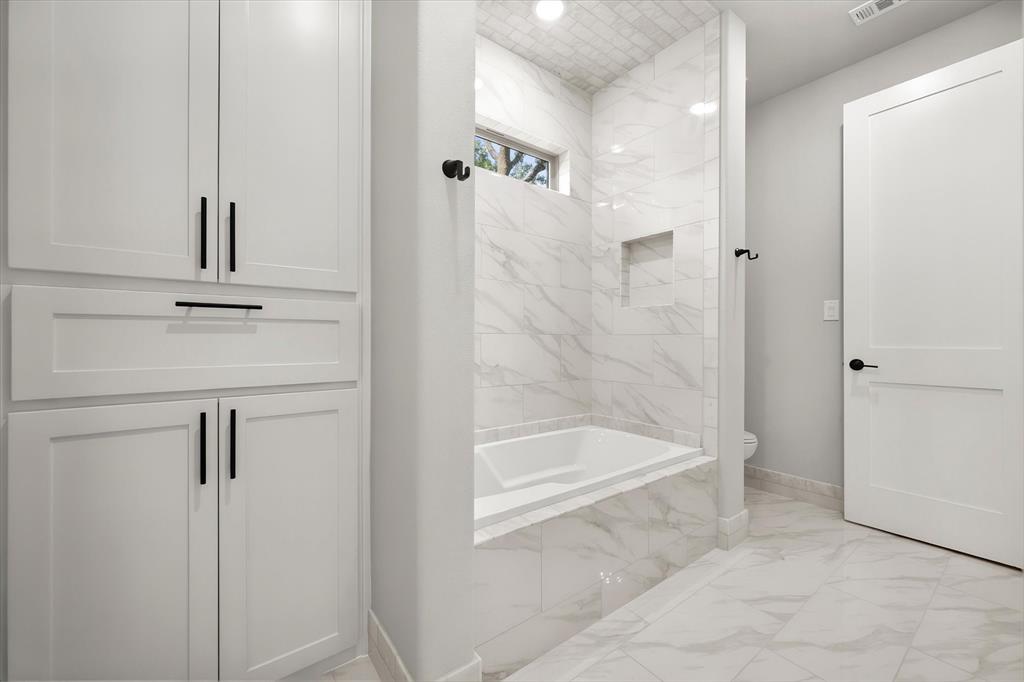 7631 Woodstream Road Midlothian, TX 76065 - Photo 35 of 40 Built-in white cabinetry with black hardware, white tile flooring, white soaking tub, and white tiled shower surround with a recessed niche