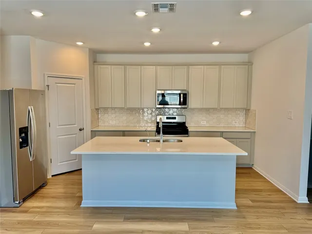 a view of a kitchen with kitchen island a sink wooden floor and stainless steel appliances