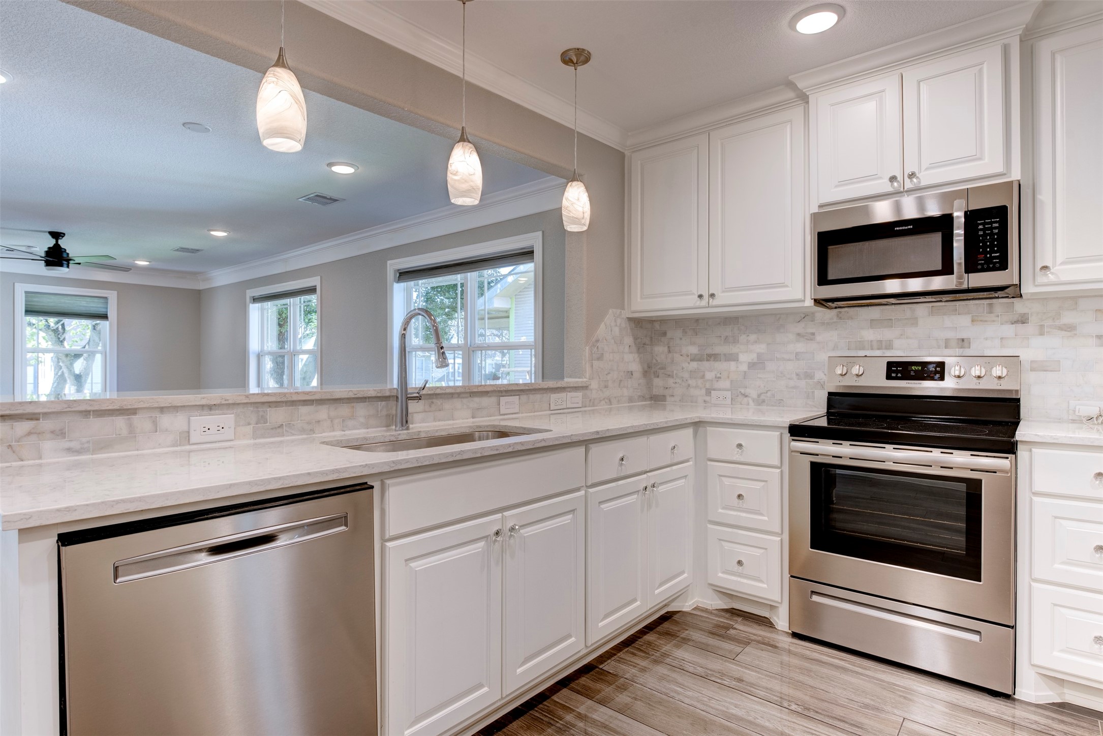 109 Dresden Street Houston, TX 77012 - Photo 17 of 43 This modern kitchen features sleek stainless steel appliances, white cabinetry, and a stylish tile backsplash. The open layout includes a breakfast bar with pendant lighting and a view into the living area, enhancing the space's bright and inviting atmosphere.