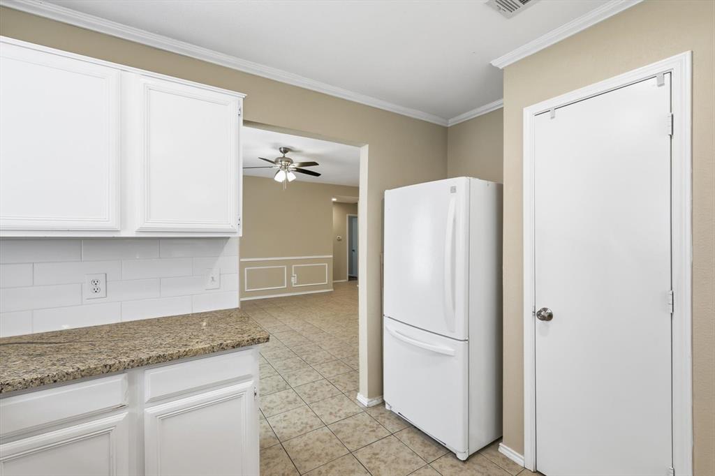 7733 Liz Lane Watauga, TX 76148 - Photo 11 of 27 Kitchen featuring freestanding refrigerator, crown molding, white cabinets, light stone counters, and light tile patterned floors
