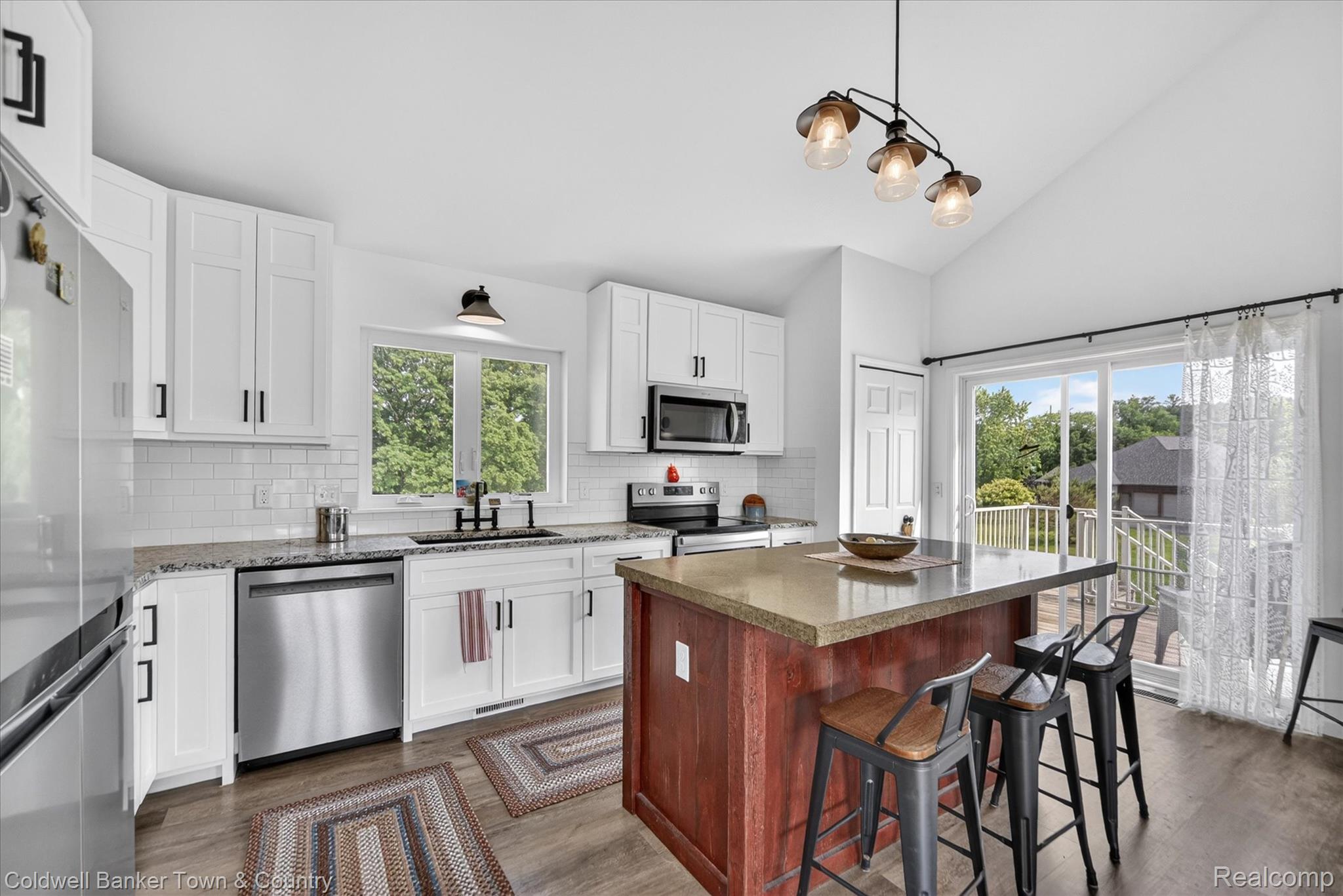 918 Gray Fox Court Howell, MI 48843 - Photo 49 of 84 Bright kitchen featuring vaulted ceilings, white shaker-style cabinetry with matte black hardware, stainless steel appliances, and a wood-finish island with a stone-finish countertop