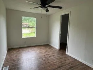 an empty room with wooden floor fan and windows