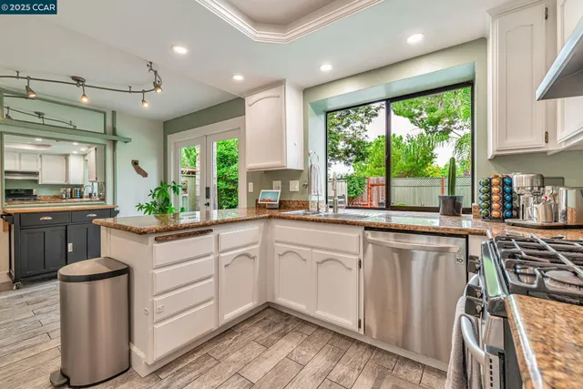 a kitchen with stainless steel appliances granite countertop a stove a sink dishwasher and white cabinets with wooden floor