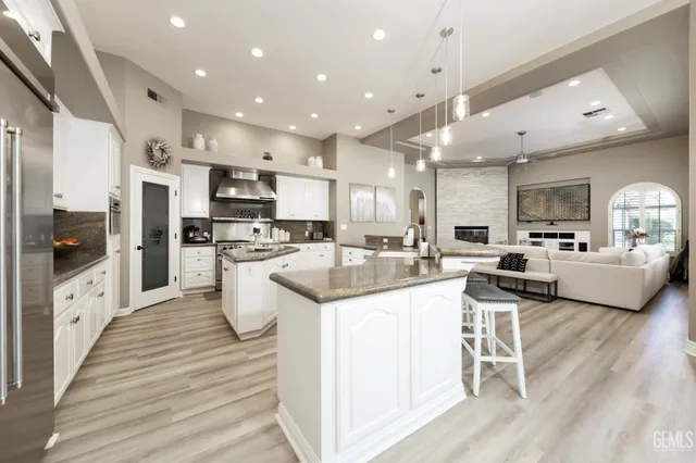 a kitchen with stainless steel appliances kitchen island granite countertop a stove top oven a sink a refrigerator and white cabinets with wooden floor
